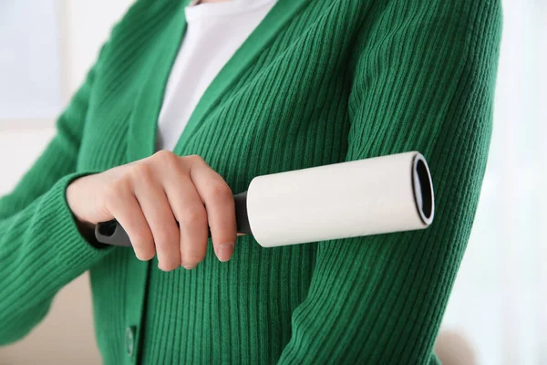 Woman cleaning green jacket with lint roller on light background, closeup
