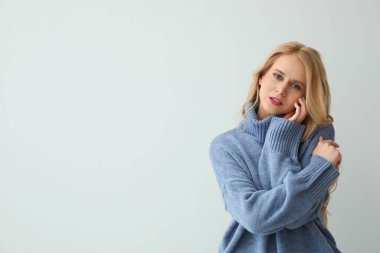Açık arkaplanda sıcak mavi süveter giyen güzel genç bir kadın. Metin için boşluk