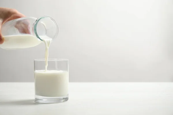 女人在白桌上把牛奶倒入玻璃杯 案文的篇幅 — 图库照片