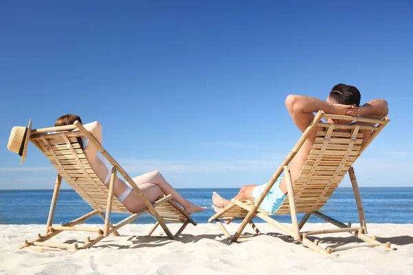 穿着比基尼的女人和她的男朋友坐在海滩的躺椅上 可爱的夫妻 — 图库照片