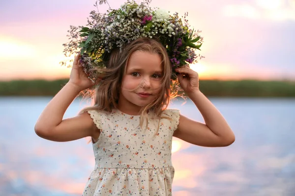 夕日の川の近くで美しい花で作られた花輪を身に着けているかわいい女の子 — ストック写真