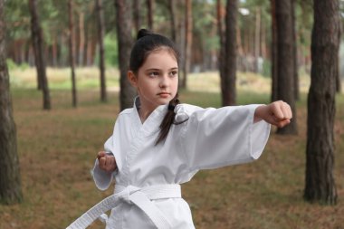 Kimonolu tatlı küçük kız ormanda karate yapıyor.