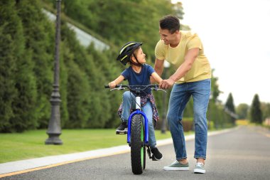 Baba oğluna dışarıda bisiklet sürmeyi öğretiyor.