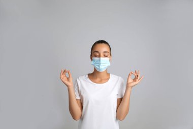 Koruyucu maskeli kadın gri arka plan üzerinde meditasyon yapıyor. COVID kaynaklı stres ile başa çıkmak mı?