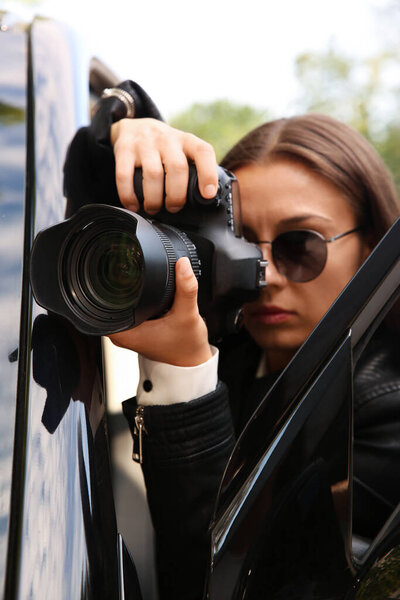 Private detective with camera spying near car outdoors