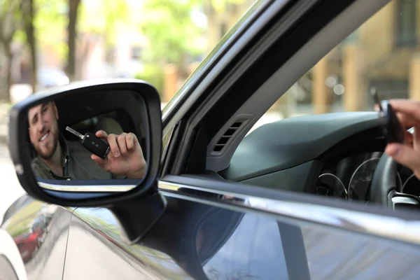 Happy man with car key in his new auto, reflection in side view mirror