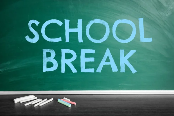 Text School Break on green chalkboard near table with chalk. Seasonal holidays