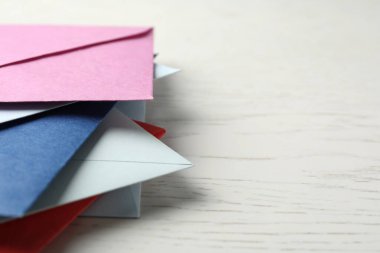 Beyaz ahşap arka planda renkli zarflar, yakın plan. Metin için boşluk