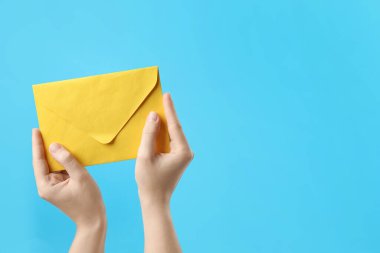 Açık mavi arka planda sarı kağıt zarf tutan kadın, yakın plan. Metin için boşluk