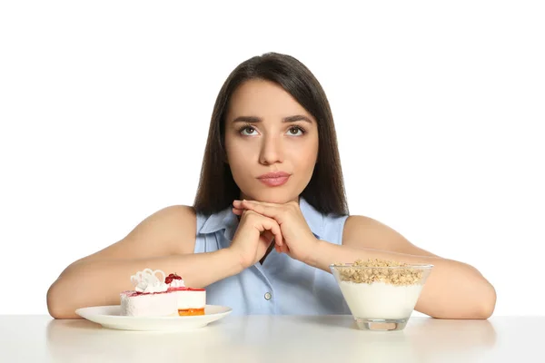白い背景にテーブルでグラノーラとケーキとヨーグルトの間で選択する疑問の女性 — ストック写真