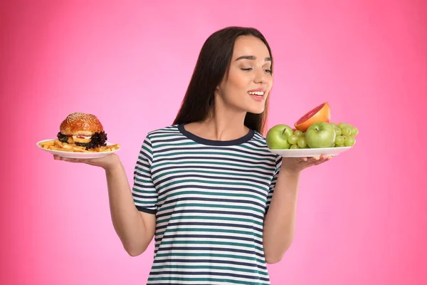 女性はピンクの背景にフランスのフライドポテトと果物やハンバーガーの間で選択 — ストック写真