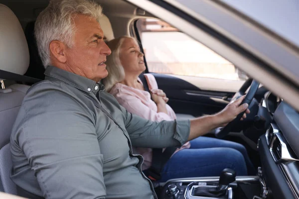 Senior man holding steering wheel while his wife having heart attack in car