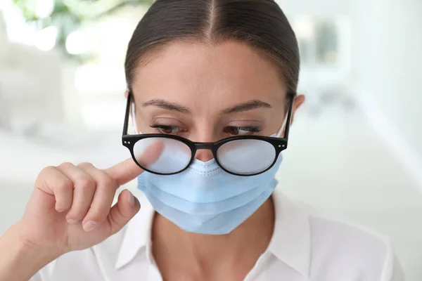 医療用マスクを室内で着用することによって引き起こされる霧の眼鏡を拭く女性は クローズアップ — ストック写真