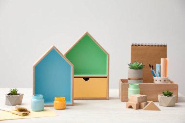 Ev şekilli raflar ve beyaz masa üzerinde boya kavanozları olan kompozisyon. İç elementler