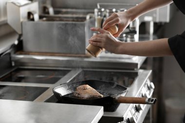 Kadın aşçı restoran mutfağında et pişiriyor, yakın plan.