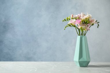 Masanın üzerinde mavi arka planda duran vazodaki güzel çiçek açan frezyalar. Metin için boşluk