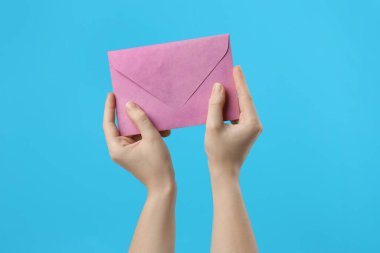 Açık mavi arkaplanda pembe kağıt zarf tutan kadın, yakın plan.