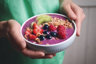 Lezzetli acai smoothie ve bulanık arka planda meyveleri olan kadın, yakın plan.