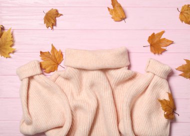 Pembe ahşap arka planda kalın süveter ve kuru yapraklar. Sonbahar mevsimi