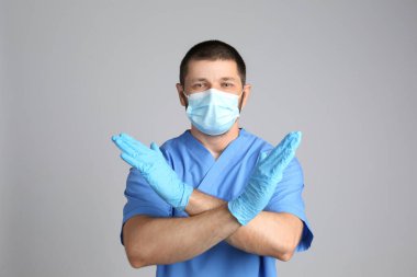 Koruyucu maskeli doktor gri arka planda dur hareketi gösteriyor. COVID 'nin yayılmasını engellemek mi?