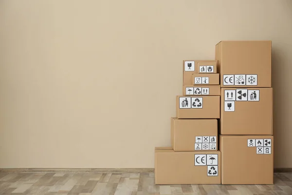 ベージュの壁 テキストのためのスペースの近くの床に異なるパッケージ記号を持つ段ボール箱 小包の配達 — ストック写真