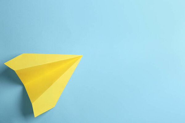 Yellow paper plane on light blue background, top view. Space for text