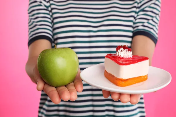 Concept of choice. Woman holding apple and cake on pink background, closeup