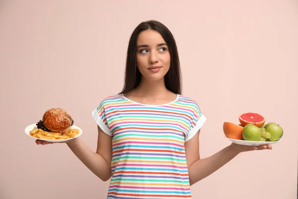 フルーツとハンバーガーの間で選ぶ女性とフランスのフライドポテトでベージュの背景 — ストック写真