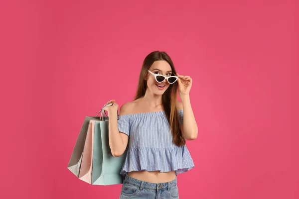 美しいです若いです女性で紙のショッピングバッグでピンクの背景 — ストック写真