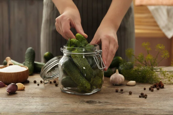 Woman putting cucumber into glass jar at wooden kitchen table, closeup. Pickling vegetables — Stock Image Woman Putting Cucumber Glass Jar Wooden Kitchen Table Closeup Pickling Stock Image