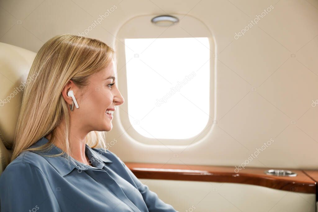 Beautiful woman listening to music via wireless earphones during flight. Air travel