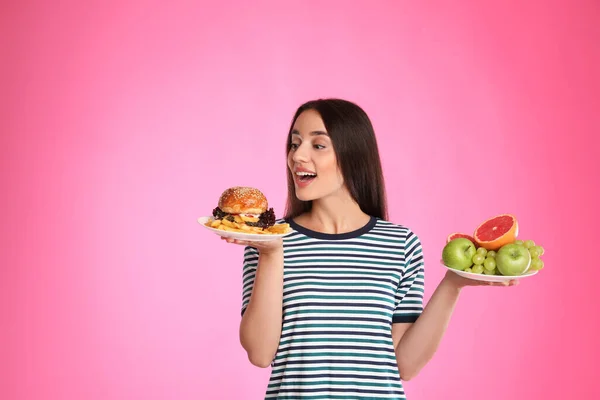 女性はピンクの背景にフランスのフライドポテトと果物やハンバーガーの間で選択 — ストック写真