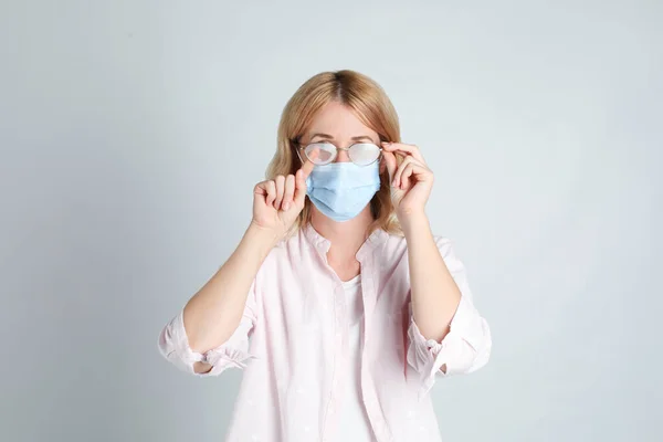光を背景に医療用マスクを着用することによって引き起こされる霧の眼鏡を拭く女性 — ストック写真