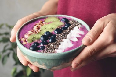 Lezzetli acai smoothie ve bulanık arka planda meyveleri olan kadın, yakın plan.