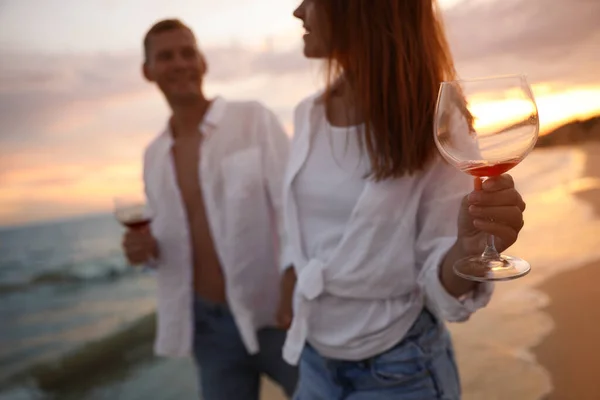 日没時に海の近くを歩きながらワインを飲むカップル ガラスと手に焦点を当てます — ストック写真