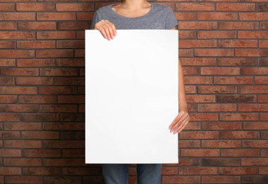 Kırmızı tuğla duvarın yanında beyaz boş poster tutan kadın, yakın plan. Tasarım için model