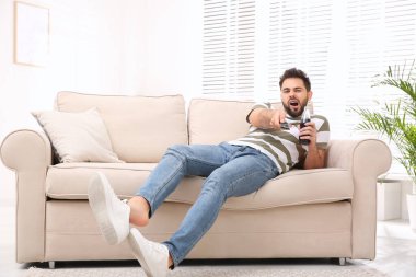 Evdeki kanepede televizyon izleyen tembel genç adam.