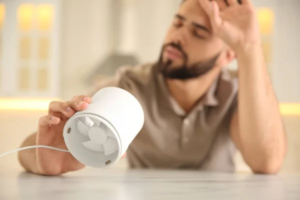 Man with portable fan suffering from heat at home, focus on hand. Summer season