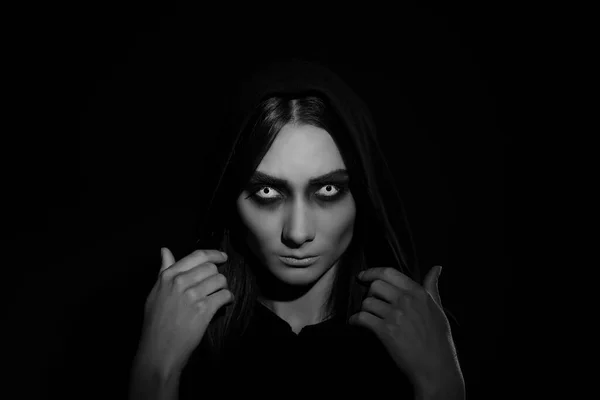 Bruxa assustadora de halloween com olhos vermelhos em um manto preto em um  ambiente sombrio