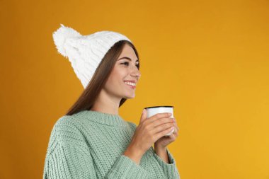 Sarı arka planda bir kupa sıcak şarapla mutlu güzel bir kadın.
