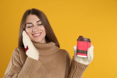 Sarı arka planda kağıt bardak sıcak şarapla mutlu güzel bir kadın.