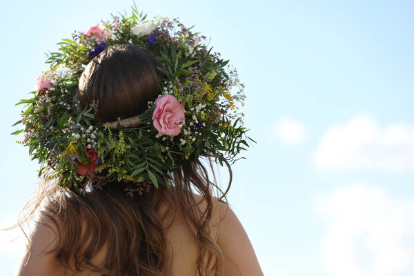 Young woman wearing wreath made of beautiful flowers outdoors on sunny day, back view