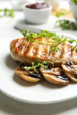 Mantarlı ızgara tavuk filetosu ve beyaz masada roka, yakın plan.