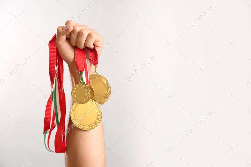 Man holding golden medals on grey background, closeup. Space for design