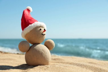 Kumsalda kumdan yapılmış, deniz kenarında Noel Baba şapkası olan bir kardan adam. Noel tatili