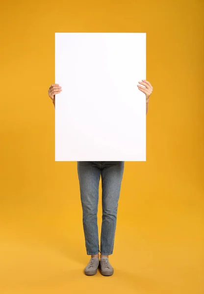 Woman holding white blank poster on yellow background. Mockup for design