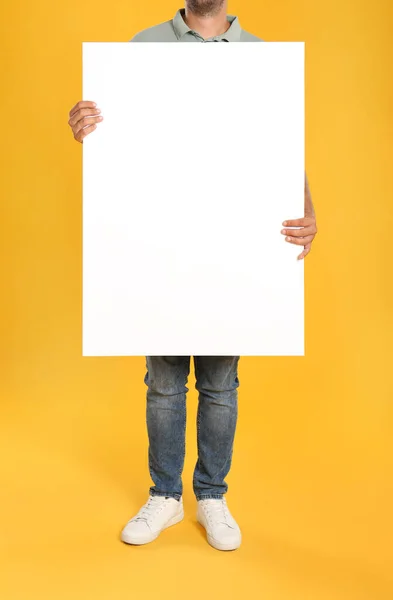 黄色の背景に白い空のポスターを持っている男を閉じます デザインのためのモックアップ — ストック写真