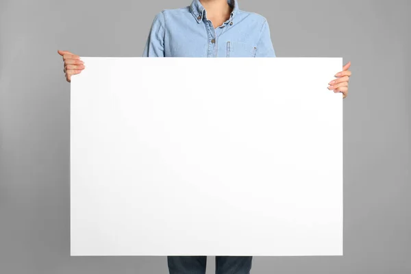 グレーの背景に白い空のポスターを持っている女性 クローズアップ デザインのためのモックアップ — ストック写真