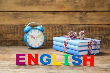Sözcük ENGLISH ahşap masa üzerinde kitap yığını ve alarm saati yanında renkli harfler ile yapılır