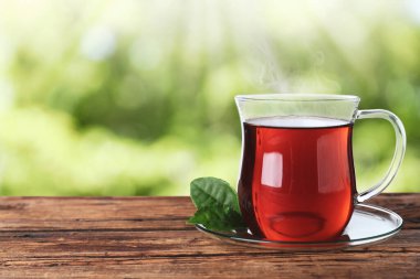 Ahşap masada, bulanık yeşil arka planda, cam bardak taze çay. Metin için boşluk